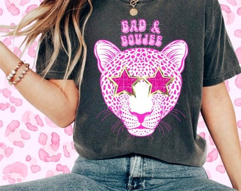 May include: A gray t-shirt with a pink leopard print design. The leopard has pink glitter stars over its eyes. The text "Bad & Boujee" is printed in pink on the shirt.