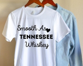 Può includere: Maglietta bianca con il testo "Smooth As Tennessee Whiskey" e un simbolo di cuore nero.