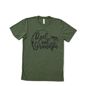 K&ouml;nnte beinhalten: Gr&uuml;nes T-Shirt mit dem schwarzen Schriftzug "Reel Cool Grandpa". Das Design zeigt eine Angelrute und einen Fisch. Das Shirt hat einen Rundhalsausschnitt und ist aus weichem Stoff.