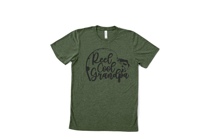 K&ouml;nnte beinhalten: Gr&uuml;nes T-Shirt mit dem schwarzen Schriftzug "Reel Cool Grandpa". Das Design zeigt eine Angelrute und einen Fisch. Das Shirt hat einen Rundhalsausschnitt und ist aus weichem Stoff.
