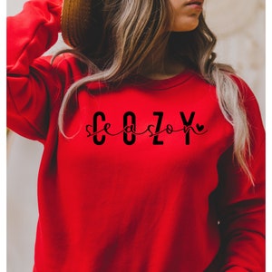 Puede incluir: Sudadera roja con el texto "Cozy season" en letras negras con un peque&ntilde;o coraz&oacute;n.