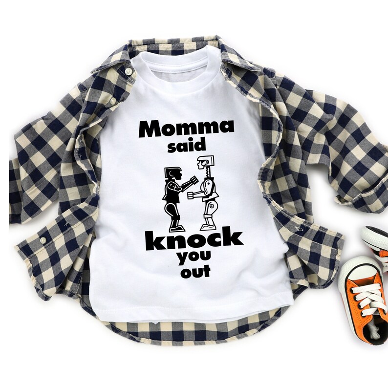 May include: White t-shirt with a black graphic of two figures boxing. The text "Momma said knock you out" is printed on the shirt.