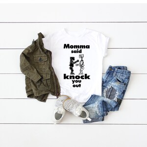 May include: White t-shirt with a black graphic of two robots fighting. The text "Momma said knock you out" is printed on the shirt.