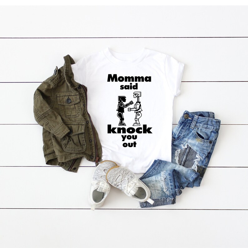 May include: White t-shirt with a black graphic of two robots fighting. The text "Momma said knock you out" is printed on the shirt.