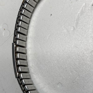 May include: A silver watch band with a repeating pattern of small rectangular links.