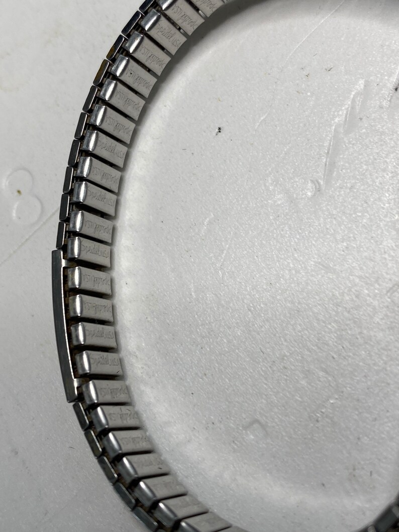 May include: A silver watch band with a repeating pattern of small rectangular links.