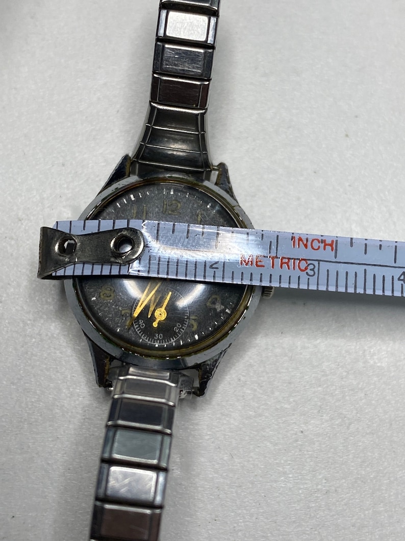 May include: A silver wristwatch with a black face and gold hands. The watch is 1 inch in diameter and has a silver metal band.