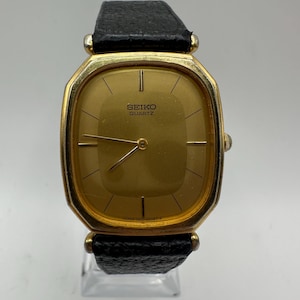 Può includere: Un orologio Seiko al quarzo dorato con quadrante quadrato e cinturino in pelle nera.