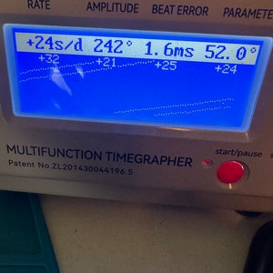 May include: A blue digital display with the text "RATE", "AMPLITUDE", "BEAT ERROR", and "PARAMETER". The display shows the following readings: "+24s/d", "242&deg;", "1.6ms", and "52.0&deg;". Below the display is the text "MULTIFUNCTION TIMEGRAPHER" and "Patent No.ZL201430044196.5".