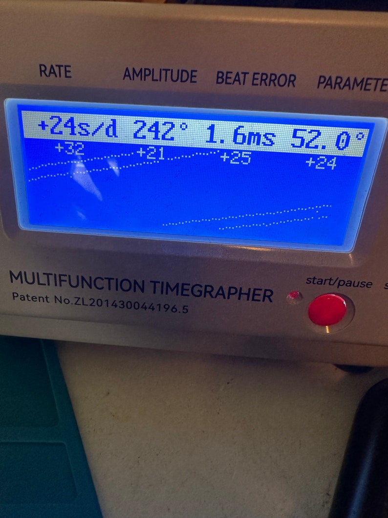 May include: A blue digital display with the text "RATE", "AMPLITUDE", "BEAT ERROR", and "PARAMETER". The display shows the following readings: "+24s/d", "242&deg;", "1.6ms", and "52.0&deg;". Below the display is the text "MULTIFUNCTION TIMEGRAPHER" and "Patent No.ZL201430044196.5".