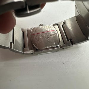 May include: Silver stainless steel watch with a rectangular face. The watch face has the words "Quick Silver" printed on it. The watch has a silver metal band.