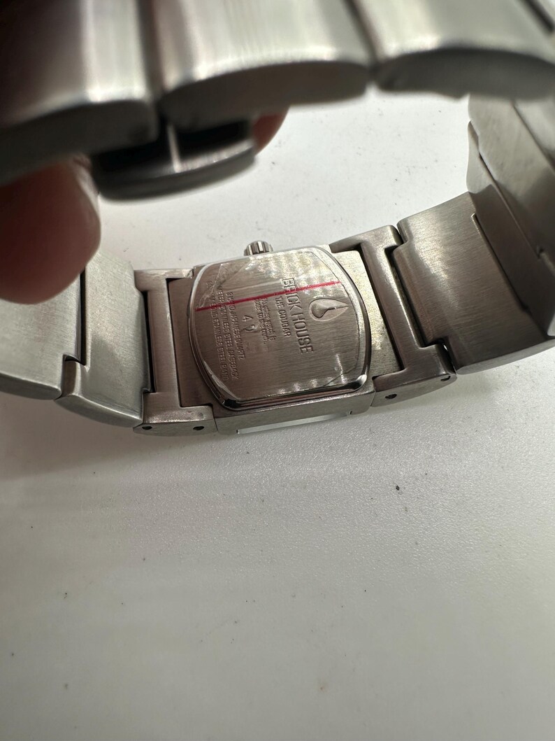 May include: Silver stainless steel watch with a rectangular face. The watch face has the words "Quick Silver" printed on it. The watch has a silver metal band.