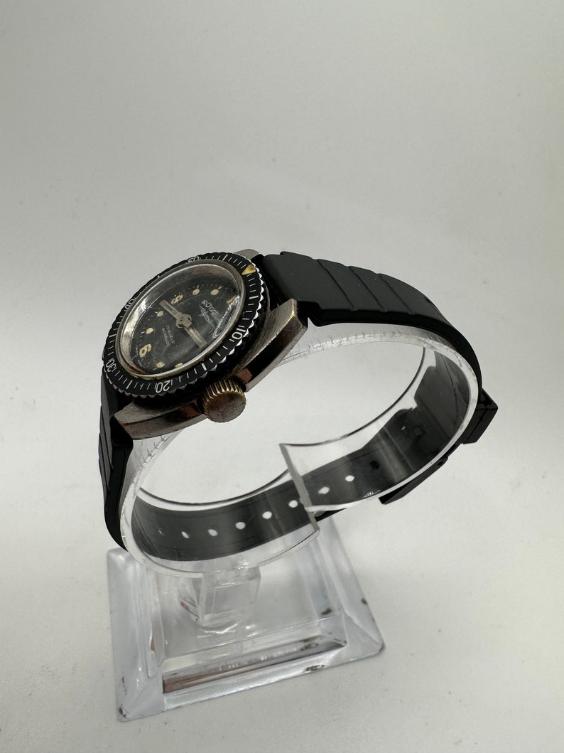 May include: A black and silver wristwatch with a black rubber strap. The watch face has a black background with white numbers and a silver second hand. The watch has a rotating bezel with white numbers.