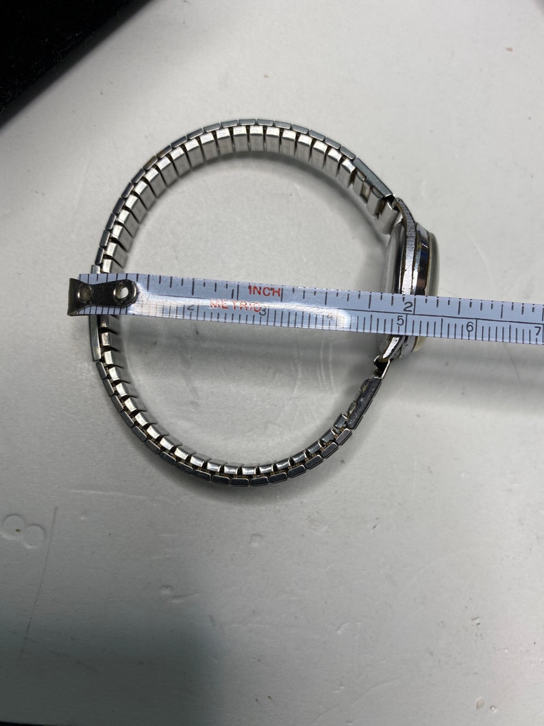 May include: A silver watch with a metal band. The band is measured with a ruler, showing it is 6 inches long.