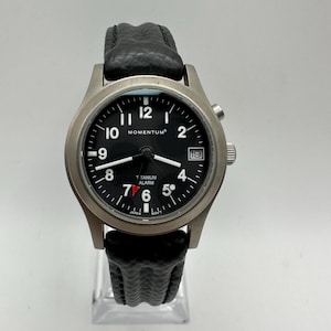 May include: A black-faced wristwatch with a silver titanium case and black leather band. The watch face has white markings for the hours and minutes, and a small date window at the 3 o'clock position. The watch also features a red alarm indicator.