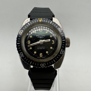 May include: A black Rotary wristwatch with a silver bezel and black rubber strap. The watch face has a black background with white markings and the text "Rotary", "17 Rubis", "Incabloc", and "Swiss Made T".