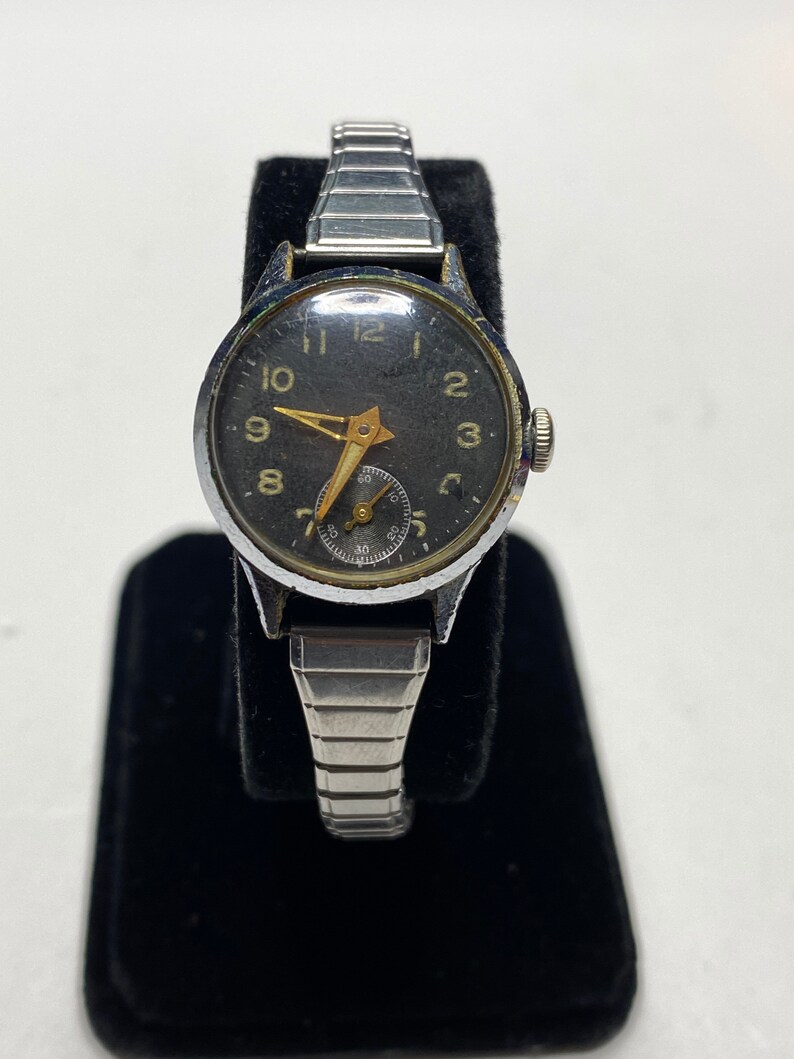 May include: A silver wristwatch with a black face and gold-colored hands and numbers. The watch has a silver metal band.