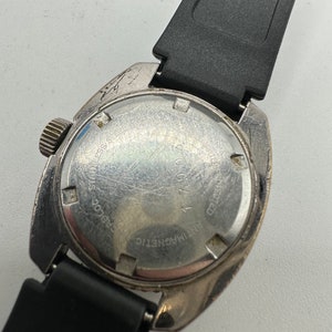 May include: The back of a silver wristwatch with a black rubber strap. The watch face has the text "Antimagnetic" and "25 Jewels" printed on it.