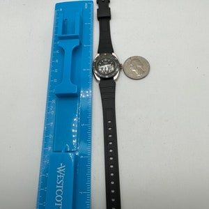 May include: A black wristwatch with a silver face and a black rubber strap. The watch has a silver bezel with a black ring around it. The watch is approximately 7 inches in length.