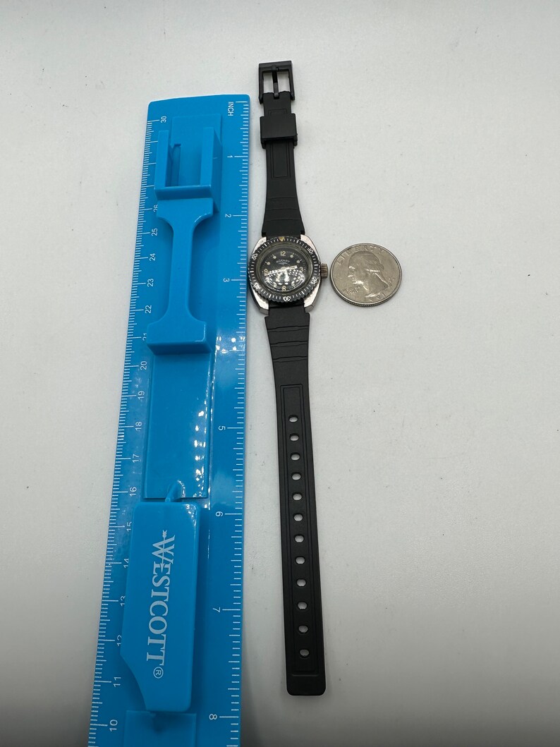 May include: A black wristwatch with a silver face and a black rubber strap. The watch has a silver bezel with a black ring around it. The watch is approximately 7 inches in length.