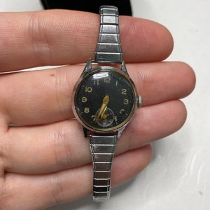 May include: A silver wristwatch with a black face and gold-colored hour markers. The watch has a silver metal band.