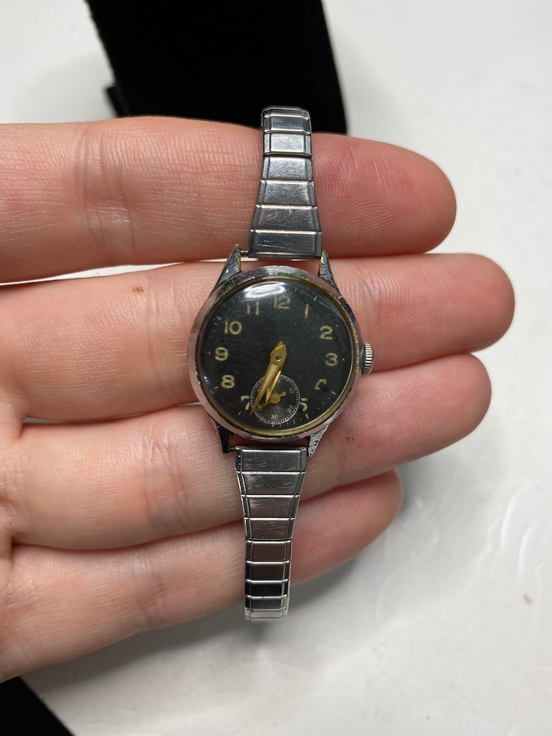 May include: A silver wristwatch with a black face and gold-colored hour markers. The watch has a silver metal band.