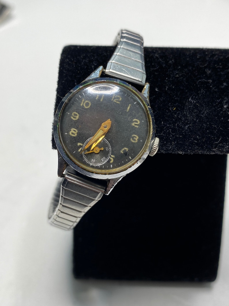 May include: A silver wristwatch with a black face and gold-colored hands. The watch has a silver metal band and a small second hand.