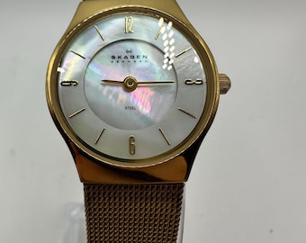 May include: A gold-tone Skagen Denmark watch with a white mother-of-pearl dial and a mesh band.