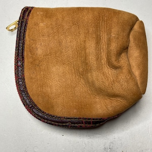 May include: A small, brown leather pouch with a zip closure and a red and brown stitched trim.