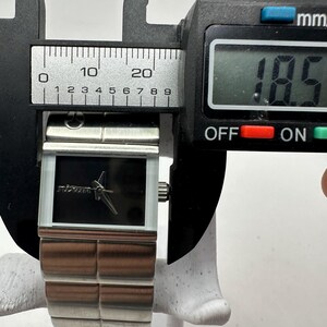 May include: A silver watch with a black face and a silver band. The watch is being measured with a caliper, which reads 18.5 mm.