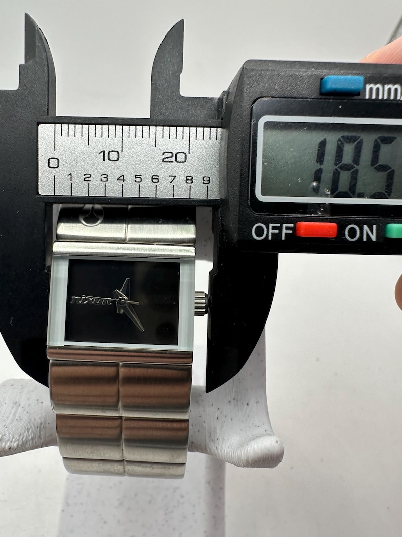 May include: A silver watch with a black face and a silver band. The watch is being measured with a caliper, which reads 18.5 mm.