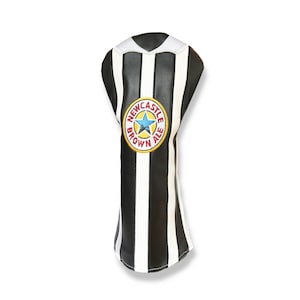 May include: A golf club head cover with a black and white striped design, featuring a Newcastle Brown Ale logo. The cover has a white collar and is made of a leather-like material.