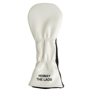 May include: White golf club head cover with black accents and the text "HOWAY THE LADS" in black. The cover is made of a soft material and has a gathered design. The cover is designed to protect golf clubs.