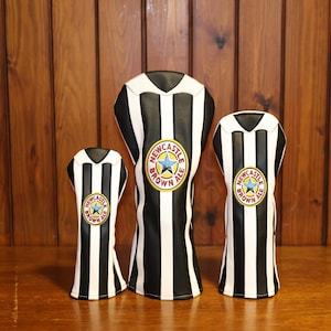 Peut inclure: Trois couvre-chefs de club de golf &agrave; rayures noires et blanches, ressemblant &agrave; un maillot. Chaque couvre-chef pr&eacute;sente un &eacute;cusson circulaire avec une &eacute;toile bleue et les mots "Newcastle Brown Ale".