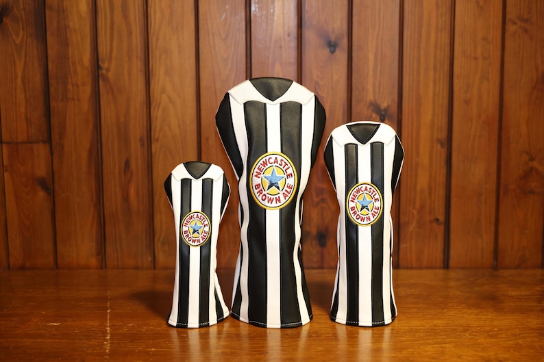 Peut inclure: Trois couvre-chefs de club de golf &agrave; rayures noires et blanches, ressemblant &agrave; un maillot. Chaque couvre-chef pr&eacute;sente un &eacute;cusson circulaire avec une &eacute;toile bleue et les mots "Newcastle Brown Ale".
