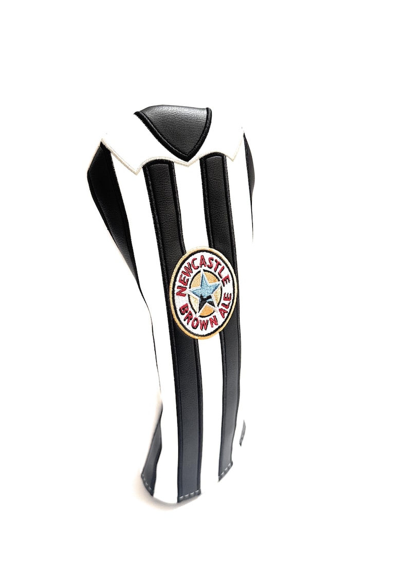 Peut inclure: Housse de club de golf &agrave; rayures noires et blanches, avec le logo Newcastle Brown Ale. La housse a un design de col et est faite d'un mat&eacute;riau durable. Le logo est circulaire avec du texte et une &eacute;toile.