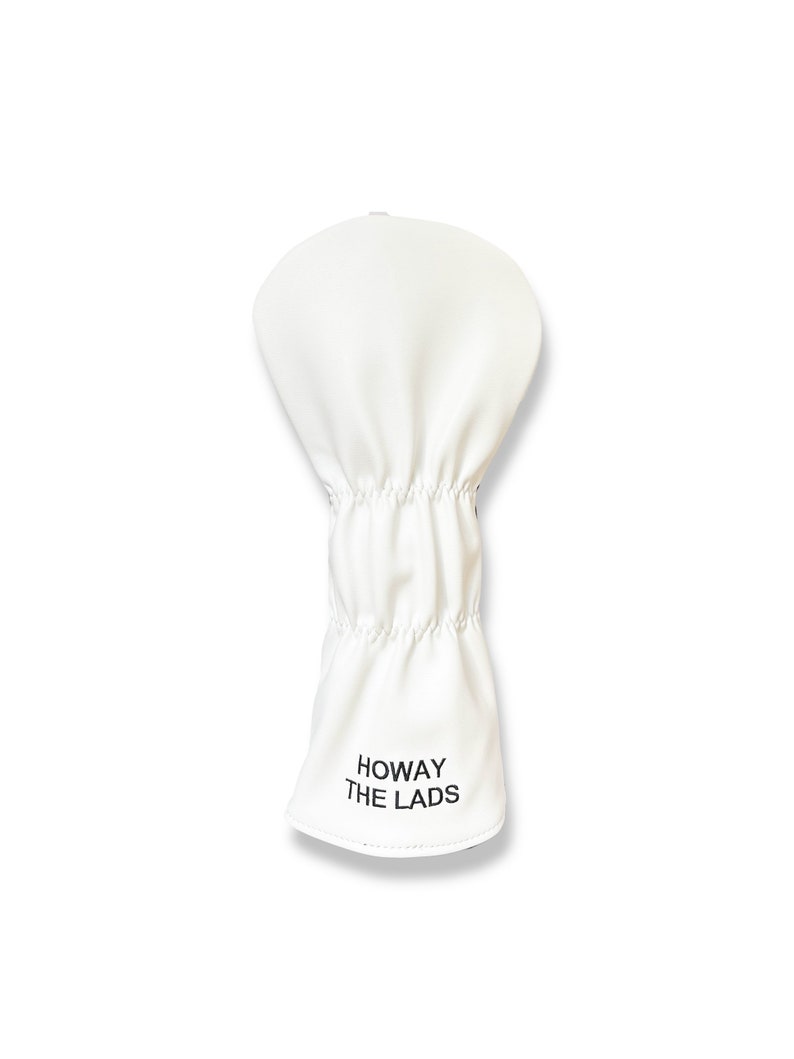 May include: A white golf club head cover with the text "HOWAY THE LADS" printed in black. The cover is made of a smooth material and has a gathered elastic section.
