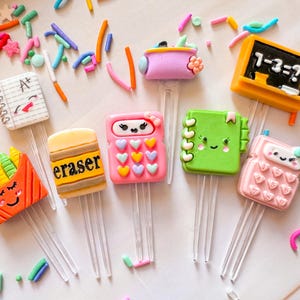 May include: Set of ten colorful bookmark clips with various school-themed designs, including a calculator, an eraser, a notebook, a chalkboard, a pencil, and a lunchbox. Each clip features a cute cartoon face.