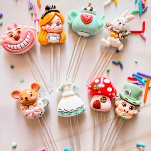 May include: Set of eight Alice in Wonderland themed cake toppers. The toppers feature characters from the book, including Alice, the Mad Hatter, the Cheshire Cat, the Queen of Hearts, and the White Rabbit. The toppers are made of polymer clay and are painted in bright colors. They are perfect for adding a whimsical touch to your next Alice in Wonderland themed party.