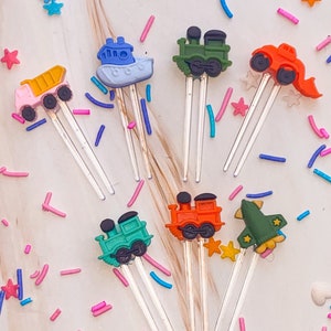 Puede incluir: Conjunto de siete adornos para pasteles coloridos que representan varios vehículos, incluyendo un tren, un camión, un barco y un cohete. Los adornos están hechos de plástico y tienen un alambre plateado unido a la parte posterior para una fácil inserción en los pasteles.