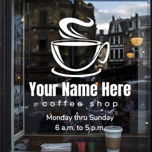 May include: A white decal on a glass window features a coffee cup with steam, and the text "Your Name Here coffee shop." Operating hours are listed as Monday thru Sunday, 6 a.m. to 5 p.m. A coffee cup is visible in the window.