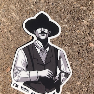 May include: A sticker featuring a black and white illustration of a man in a wide-brimmed hat and vest. The text "I'M YOUR HUCKLEBERRY" is printed in black on the bottom of the sticker. The man has a mustache and is wearing a patterned tie.