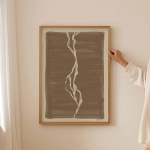 Puede incluir: Una impresión de arte abstracto enmarcada con un fondo marrón y un diseño de líneas blancas. La impresión está en un marco de madera.