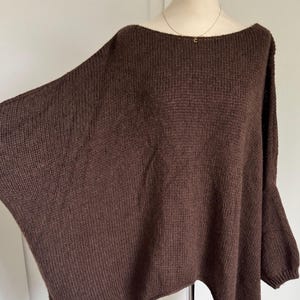 Könnte beinhalten: Ein brauner, übergroßer Strickpullover mit Bootsausschnitt. Der Pullover hat lange Ärmel und eine lockere Passform. Der Stoff scheint ein weiches, strukturiertes Strickmaterial zu sein. Der Pullover wird auf einer Schaufensterpuppe präsentiert.