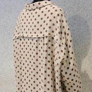Könnte beinhalten: Beige Hemd mit braunen Polka Dots. Das langärmlige Hemd hat einen Kragen und eine Knopfleiste. Der Stoff hat eine strukturierte Optik, und das Kleidungsstück wird präsentiert.