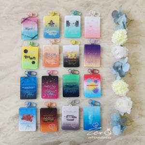 May include: A collection of rectangular keychains with various designs and text, including "Magnet," "マトリョシカ," and "MESMERIZER." Each keychain has a metal clasp and a gradient color scheme, with some featuring illustrations and handwritten-style text. The background includes floral decorations.