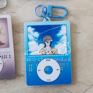 May include: A blue acrylic keychain featuring an anime character design. The keychain has a blue frame with a sky background and a character illustration. The text "zerii-charrd.co" is visible. Includes a blue metal clasp.