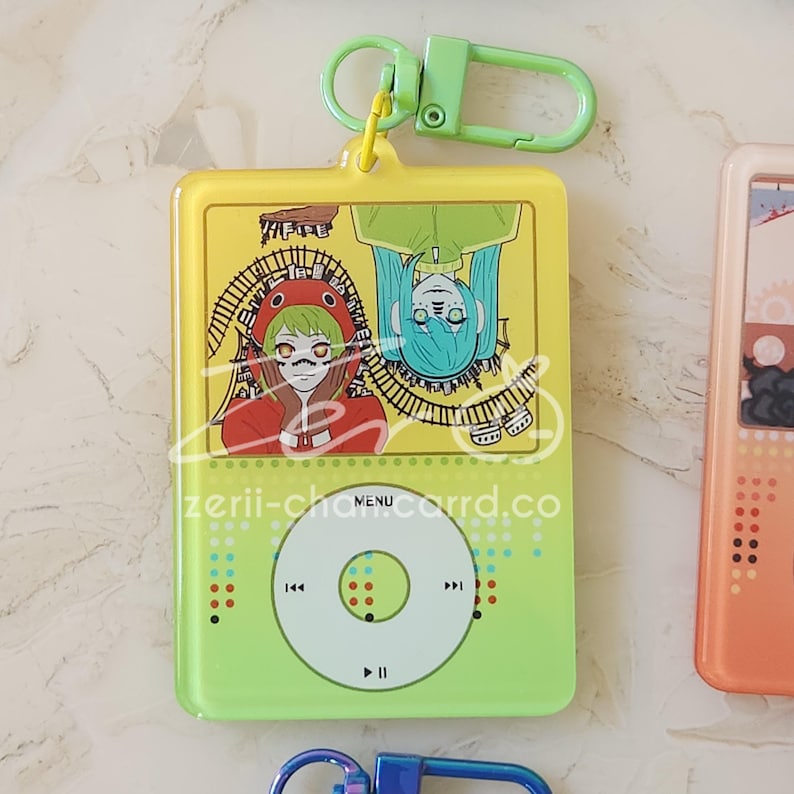 May include: A yellow and green acrylic keychain with a cartoon design. The keychain features a design of two characters and the text "zerii-chancord.co". The keychain has a green clasp.