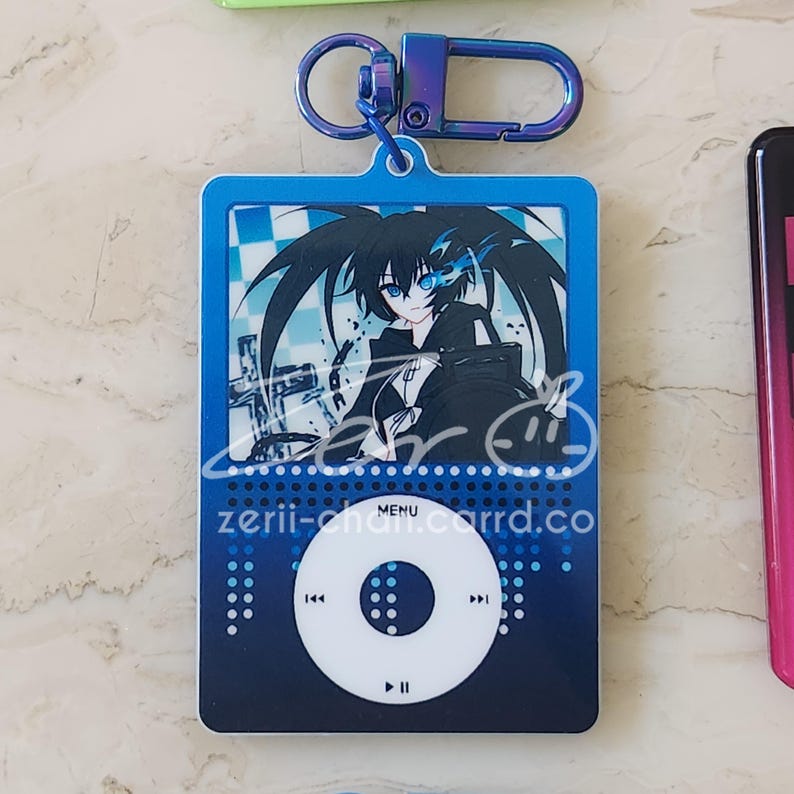 May include: A blue keychain featuring a stylized anime character design. The keychain has a blue carabiner clip and a rectangular pendant with a character illustration, a circular control design, and the text "zerii-chan.carrd.co".