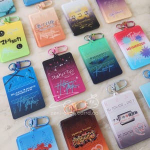 May include: A collection of rectangular keychains in various colors, including blue, pink, and orange. Each keychain features unique graphic designs and text in multiple languages, with attached metal clasps for easy attachment.